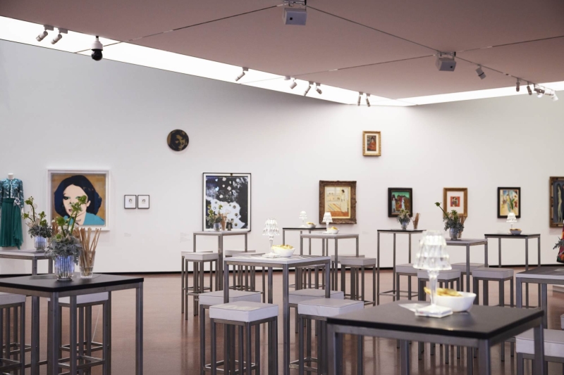 Moderne Galerie mit Tischen, Kunstwerken an Wänden und floralen Arrangements in Vasen.