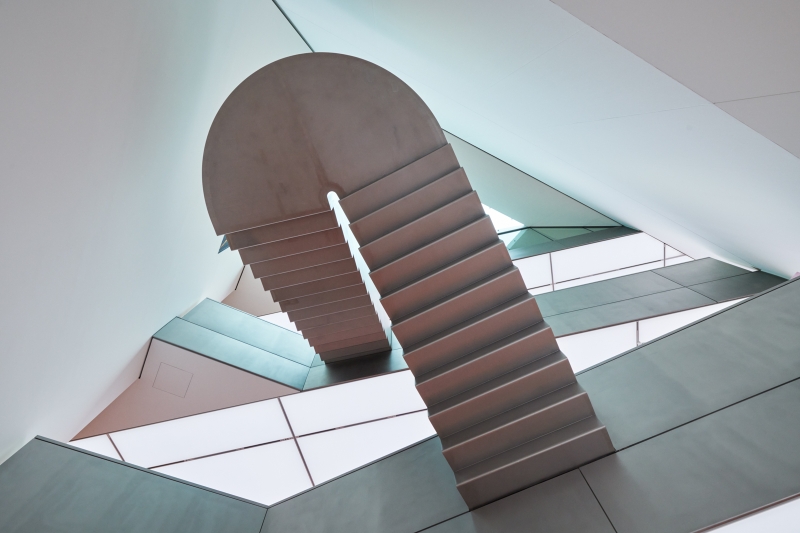 Architektonische Treppe mit geschwungener Form und modernen, hellen Wänden in einem lichtdurchfluteten Raum.