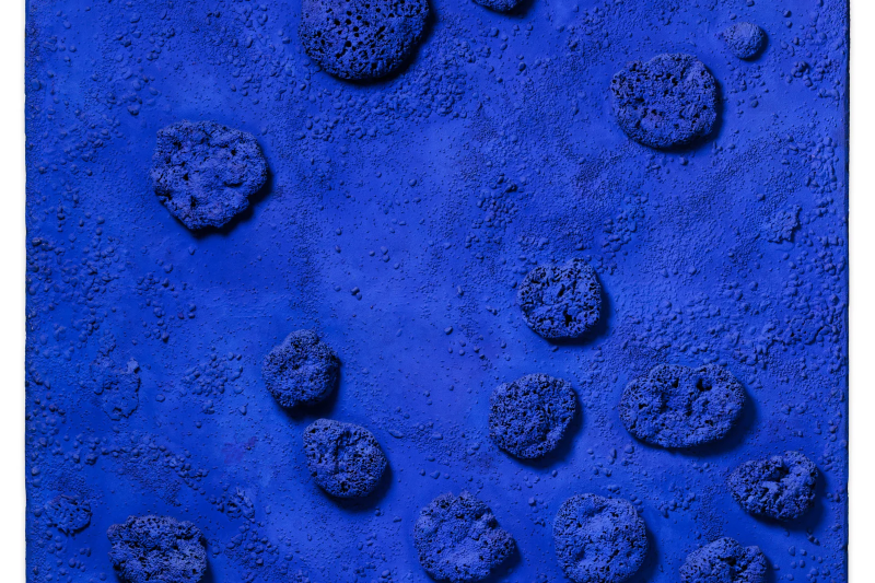 Das Kunstwerk ist ein rechteckiges Relief – also eine Art Bild mit dreidimensionalen Formen. Es ist ganz in intensivem Ultramarinblau gehalten, einer Farbe, die Yves Klein berühmt gemacht hat. Diese Farbe wirkt leuchtend, tief und fast körperlich – als würde sie Licht in sich aufnehmen.

Auf der Fläche sind echte Naturschwämme und kleine Kieselsteine befestigt. Sie sind unregelmäßig verteilt und ragen aus der Oberfläche heraus. Manche sind rundlich, andere eher flach oder porös. Die Schwämme werfen feine Schatten, je nach Lichteinfall – das gibt dem Werk eine lebendige, bewegte Struktur.

Die Fläche selbst ist nicht glatt, sondern leicht körnig und rau. Auch dort sieht man kleinere Erhebungen, die wirken, als hätte sich die Farbe natürlich über den Untergrund gelegt, wie Sand, der sich am Meeresboden sammelt.

Die Schwämme sind vollständig mit Yves Kleins spezieller blauer Farbe getränkt – sie sehen fast wie kleine Himmelskörper oder Tiefseetiere aus. Obwohl das Werk keine Figur zeigt, wirkt es organisch und lebendig.