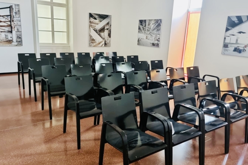 Schwarze Stühle stehen in einem Raum mit großen Fenstern und Bildern an den Wänden.
