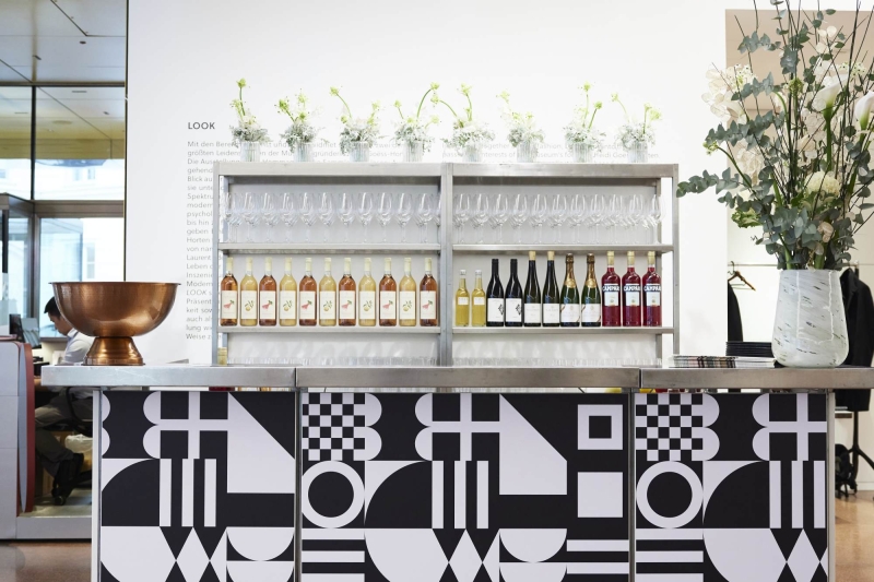 Moderne Bar mit geometrischen Mustern, Gläsern und Flaschen, dekoriert mit Blumenarrangements.