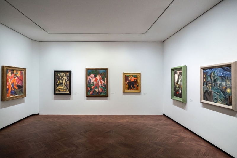 The photo shows a room from the “Experiment Expressionism” exhibition.
The room is bright, with white-painted walls and a brown wooden floor.
Six paintings hang on the walls.
The paintings show people in motion, naked bodies, strong colors and special poses - typical of Expressionism.