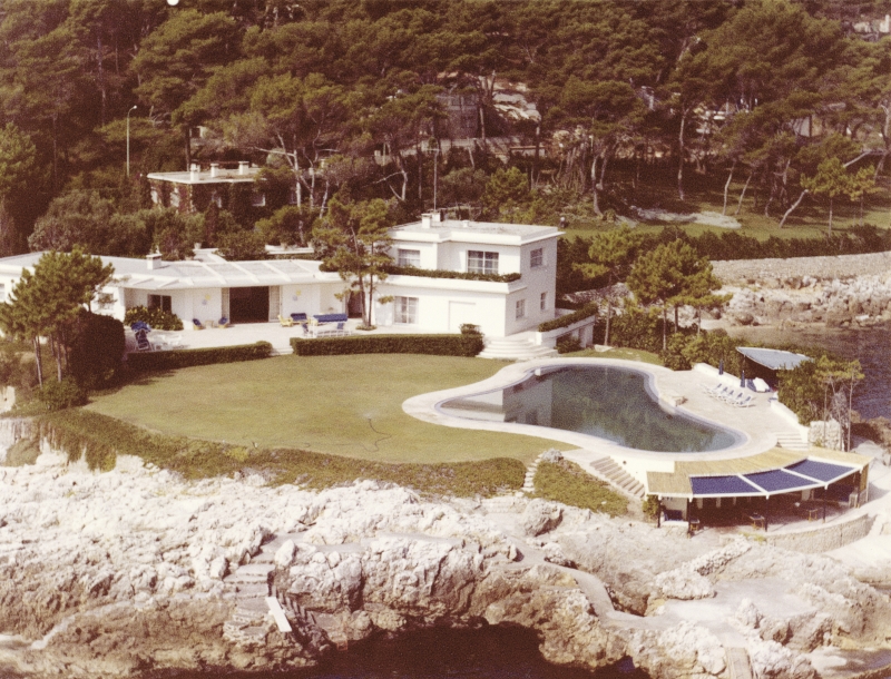 Moderne Villa mit Pool, großzügiger Rasenfläche und umgeben von Bäumen, direkt am Wasser gelegen.