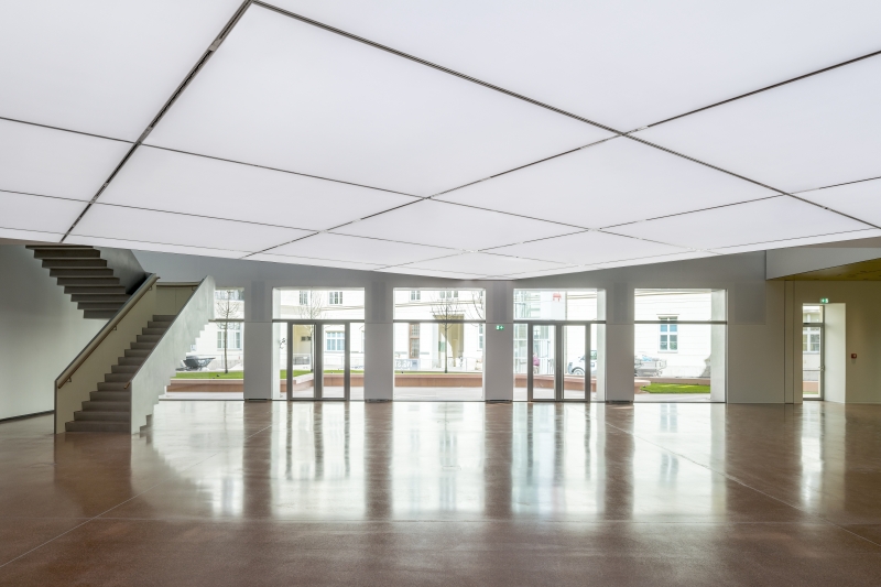 Heller, moderner Innenraum mit großen Fenstern, Treppe und glänzendem Boden.