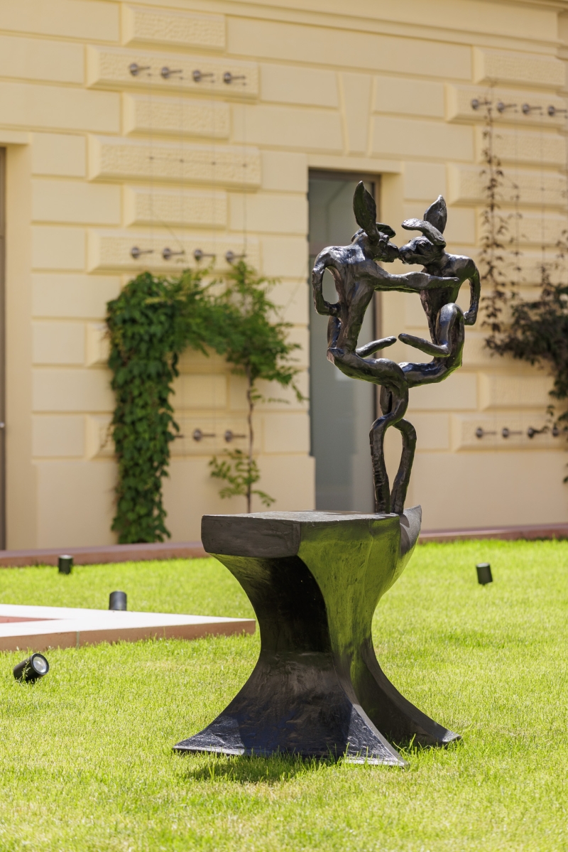 This artwork is by Barry Flanagan, an artist from Wales who has often made bronze hares. The sculpture shows a large, heavy anvil - a tool that was once used for forging. On this anvil stands a funny, playful rabbit figure. The rabbit looks as if it is dancing or making a crazy movement. Its long ears are sticking up and its arms and legs are greatly exaggerated.
Barry Flanagan liked to make characters that show imagination and have a bit of humor. For him, the rabbit is not a normal animal, but rather a symbol of lightness, creativity and fun. The strong contrast between the heavy, solid anvil and the moving, light hare makes the work particularly interesting. It shows that art does not always have to be serious - it can also surprise, delight and make people smile.
The material is dark bronze. It looks noble and heavy, but fits in well with Flanagan's playful style. The sculpture stands outside in a meadow. There it comes to life even more because the light, shadows and surroundings change. The hare almost seems as if it is about to hop off.
Translated with DeepL.com (free version)