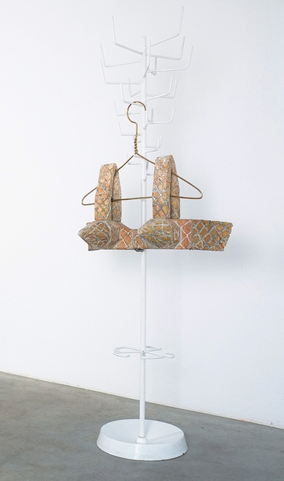 Kleiderständer mit einem kunstvollen, gemusterten Oberteil in sanften Farben vor einer weißen Wand.