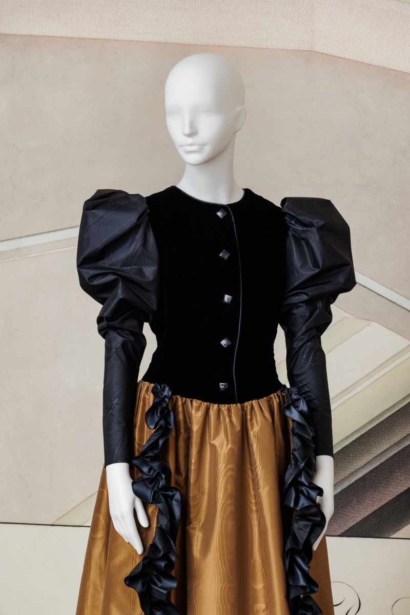 Schwarzes Kleid mit Puffärmeln und goldener, rüschierter Rockpartie, präsentiert an einer weißen Schaufensterpuppe.
