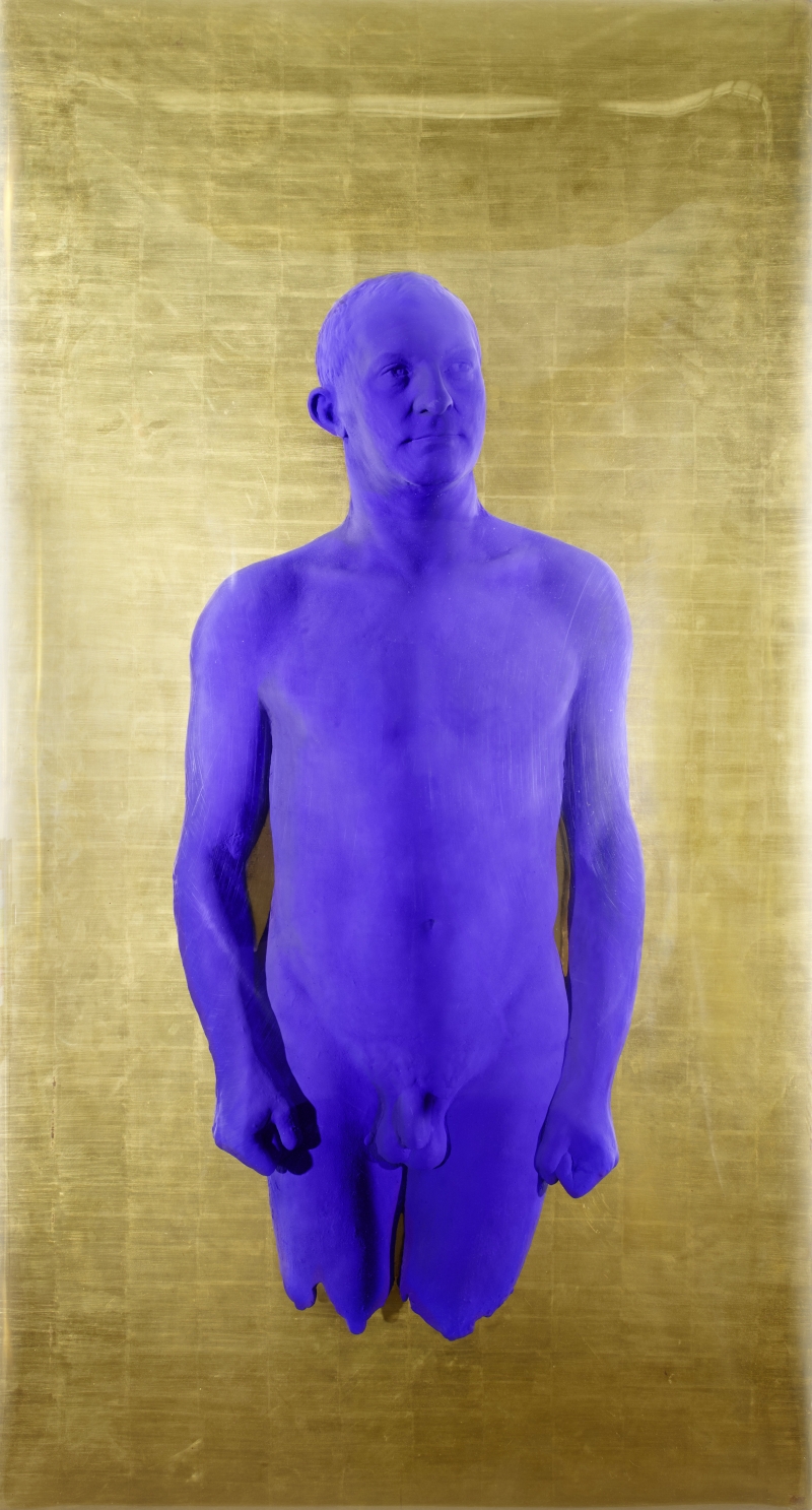 A life-sized, purple human figure stands against a gold background, with a neutral expression and arms at its sides.
