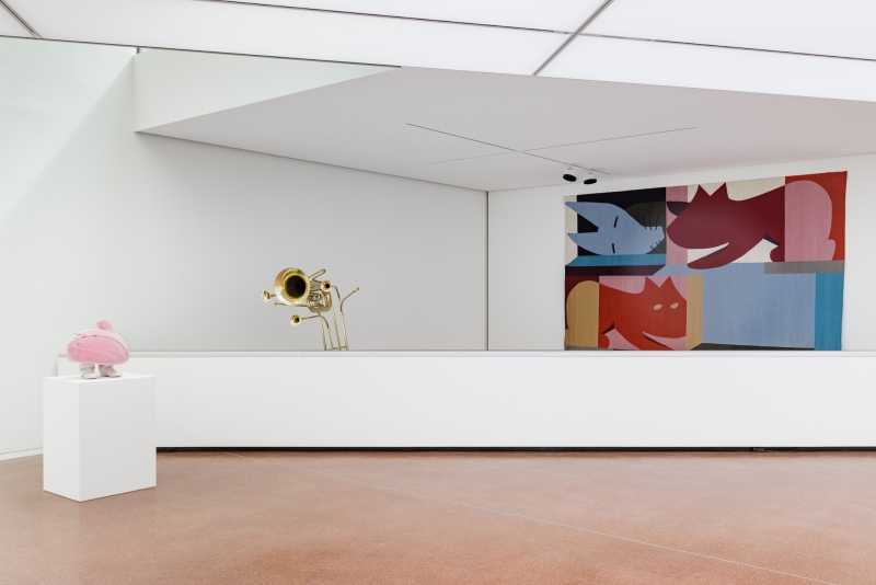 Moderne Galerie mit einer rosa Skulptur, einer goldenen Trompete und einem farbenfrohen Wandbild.