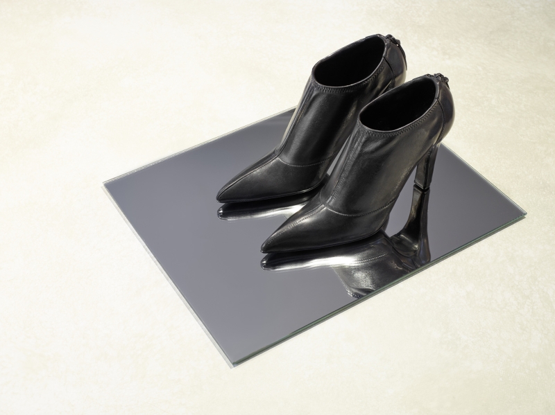 Schwarze High Heels mit spitzen Zehen auf einem spiegelnden Untergrund.