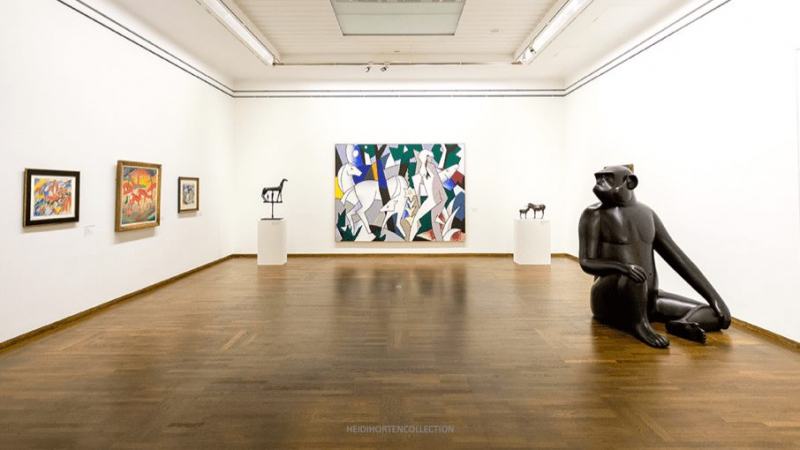 Art gallery interior featuring colorful paintings, a large abstract artwork, and a black monkey sculpture on the floor.