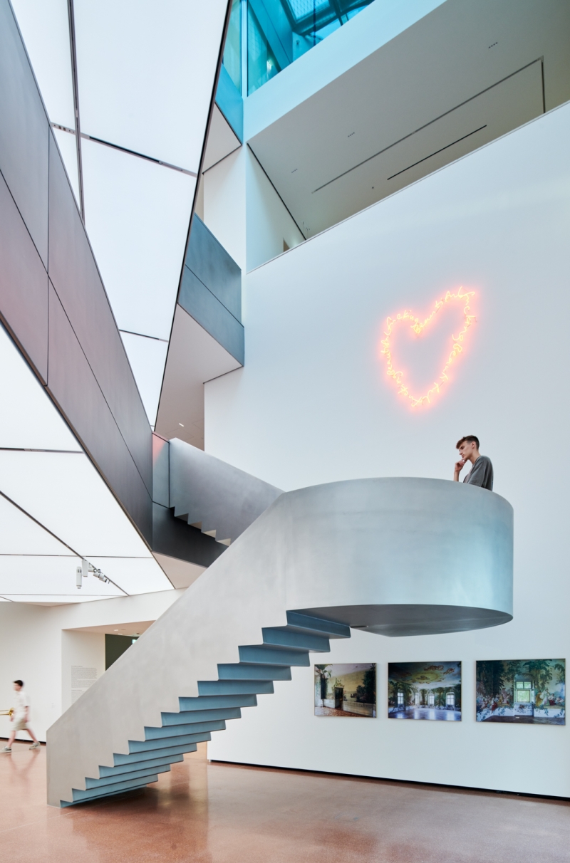 A modern staircase curves upward, with a neon heart installation on the wall and framed artworks nearby.