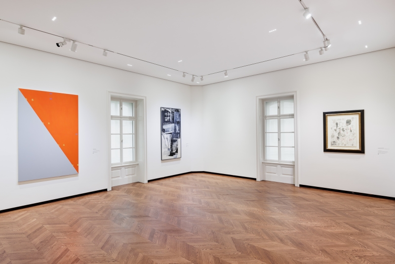 Moderne Galerie mit drei Kunstwerken an weißen Wänden und Holzfußboden, Fenster mit natürlichem Licht.