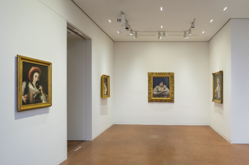 Ausstellungsraum mit vier Gemälden in goldenen Rahmen an weißen Wänden und einem braunen Boden.