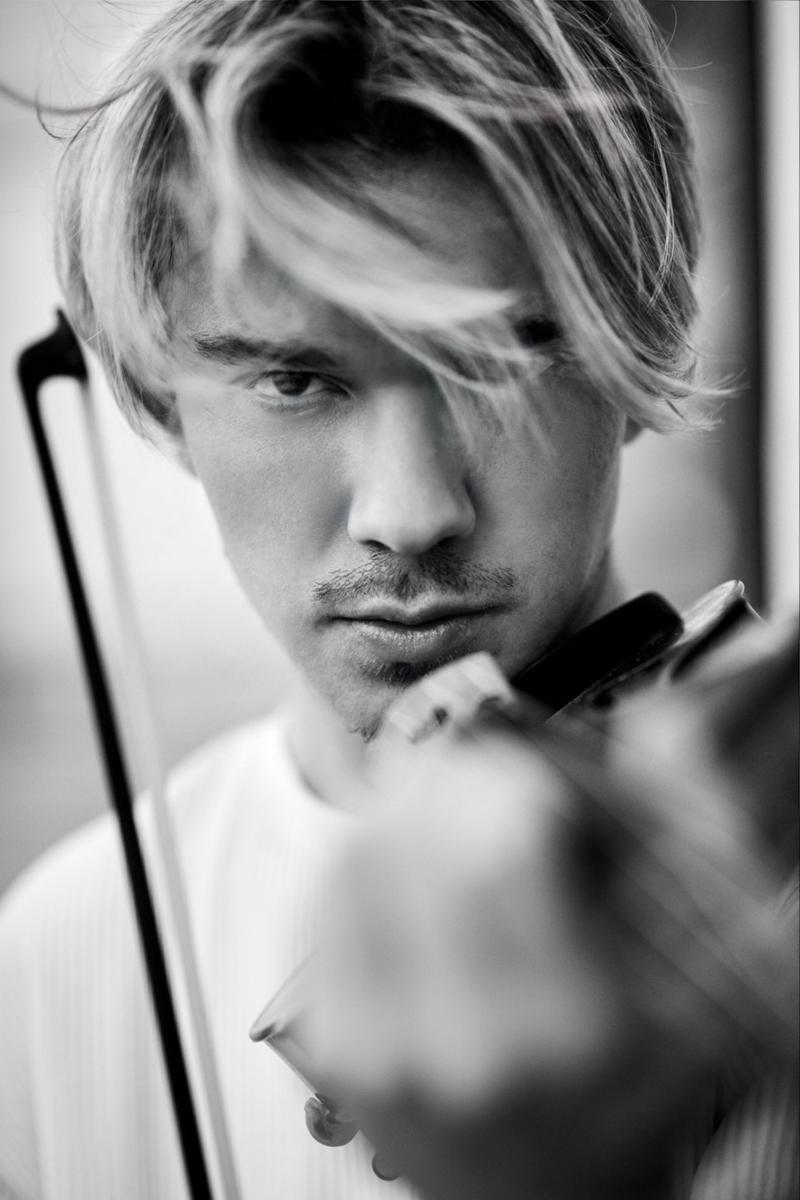 Junger Mann mit blonden Haaren spielt Geige, intensiver Blick, schwarz-weiß Fotografie.