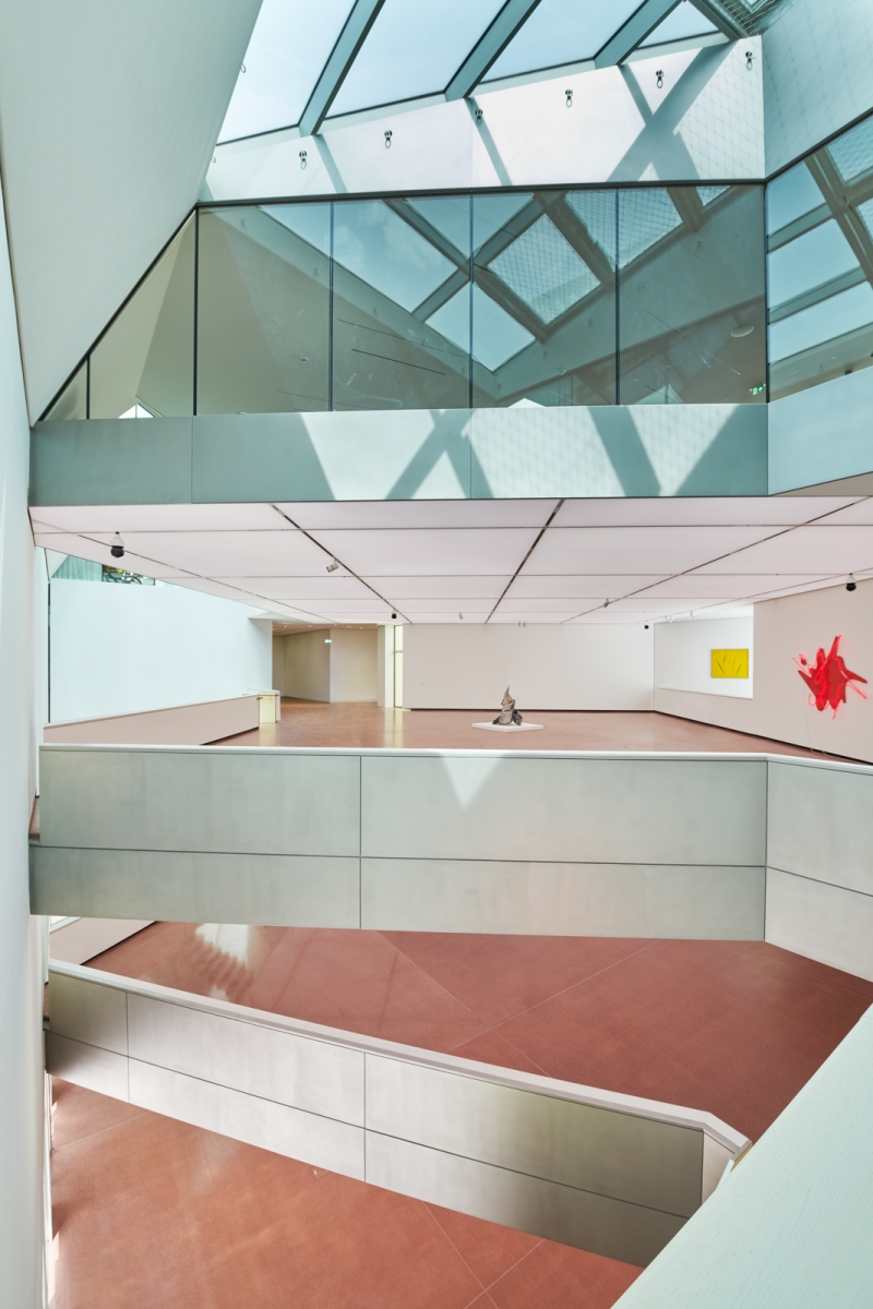 Modern art gallery interior with glass walls, skylights, and abstract sculptures on polished floors.