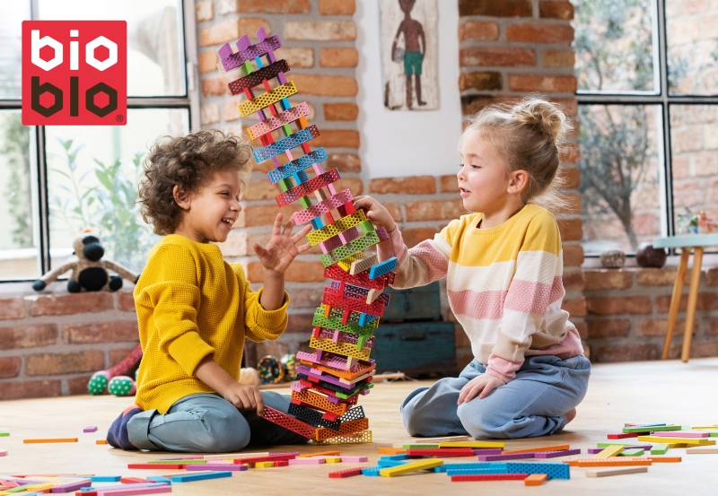 Ein Mädchen und ein Junge bauen einen Turm aus bunten Bioblo Steinen