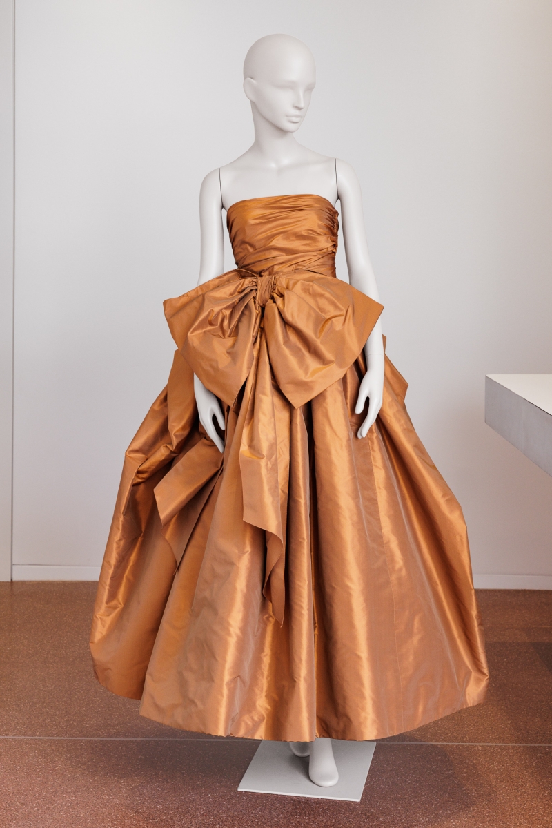 Braunes, schulterfreies Abendkleid mit voluminösem Rock und großer Schleife, präsentiert an einer weißen Schaufensterpuppe.