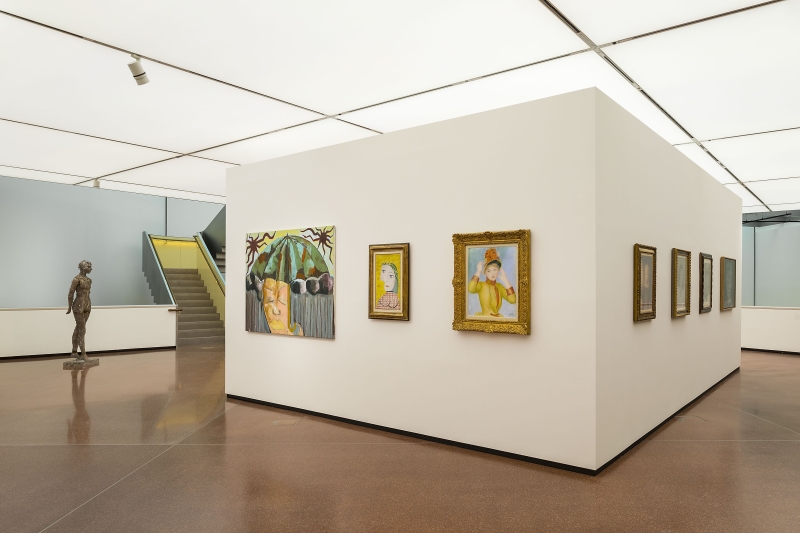Moderne Galerie mit weißen Wänden, Skulptur und mehreren Gemälden in goldenen Rahmen. Treppe im Hintergrund.