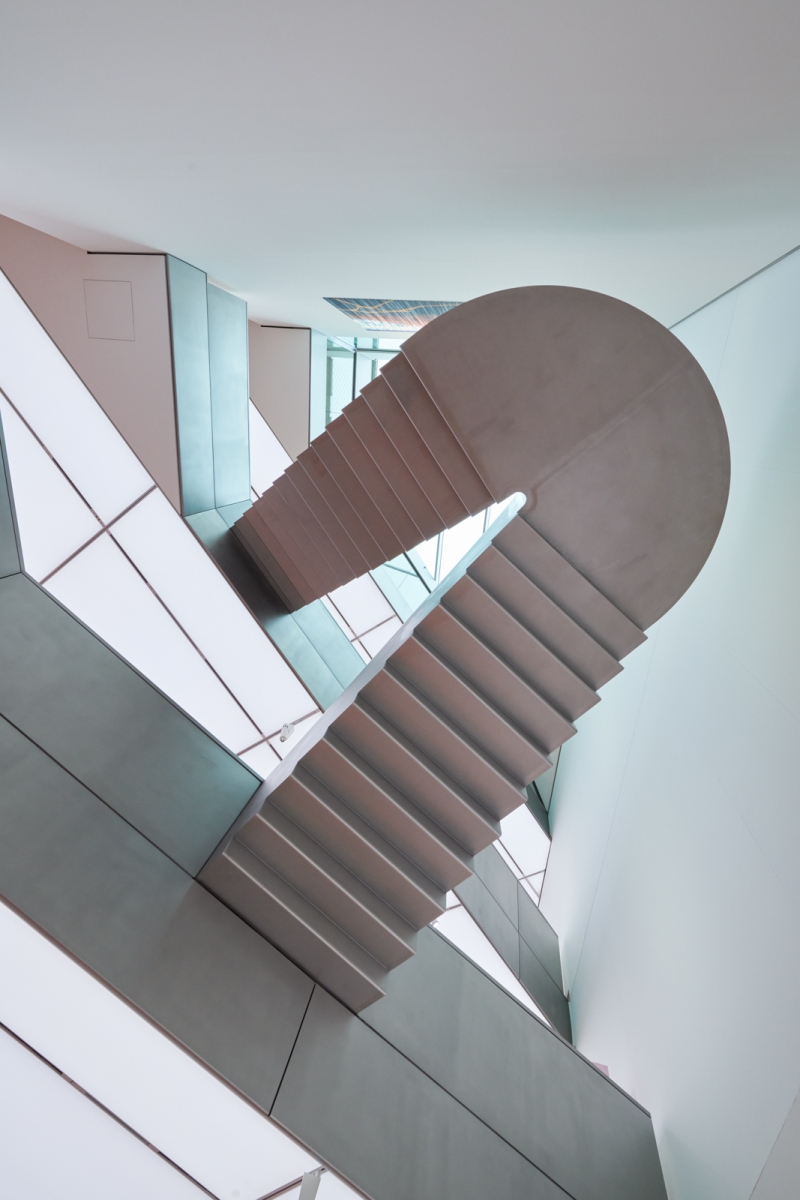The picture shows a floating staircase inside the Heidi Horten Collection in Vienna.
It connects two floors of the museum.
The walls and ceilings are white and modern in design.
There are large windows through which daylight enters.
Everything looks bright, calm and clear.