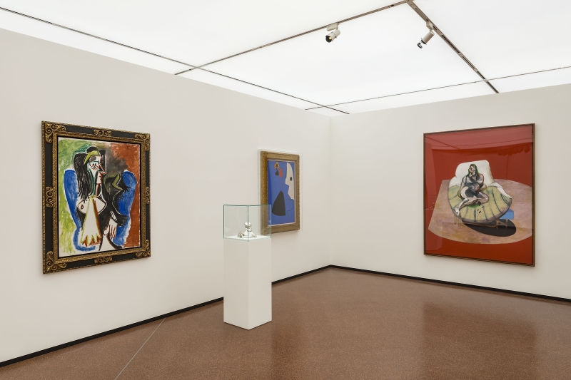 Ausstellungsraum mit zwei Gemälden an Wänden, einer Skulptur in Vitrine und einem neutralen Bodenbelag.
