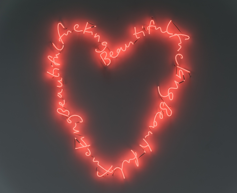Neonlicht in Herzform mit der Aufschrift „Fucking Beautiful“ in leuchtendem Rot auf grauem Hintergrund.