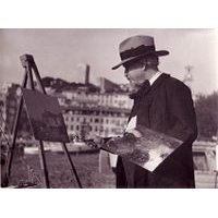 Artist in a hat painting at an easel, with a waterfront cityscape in the background.