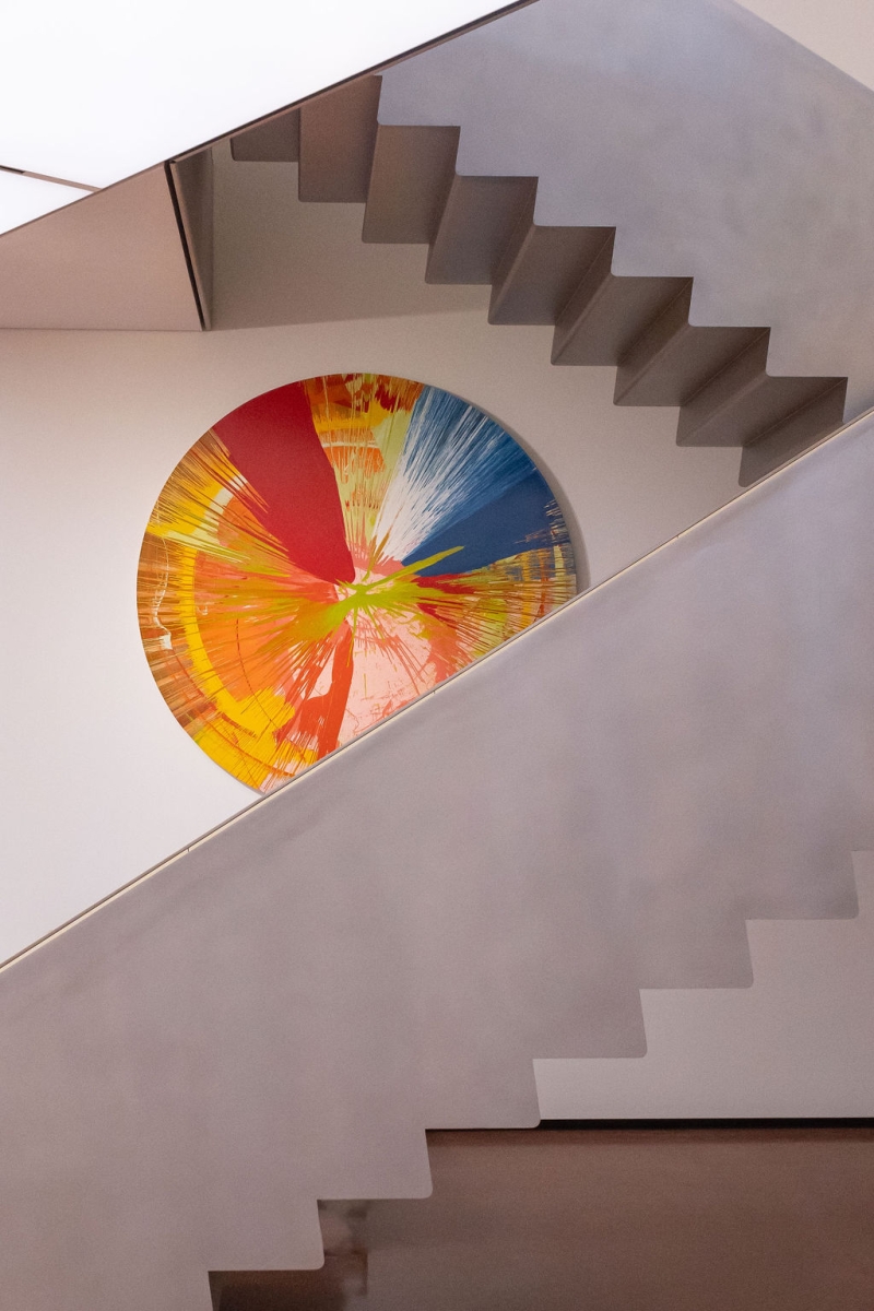 Colorful circular artwork hangs on a wall beside a modern, minimalist staircase with angular steps.
