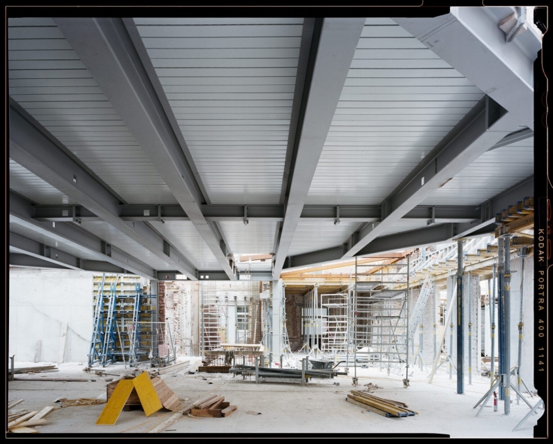 Blick auf eine Baustelle mit Stahlträgern, Gerüsten und Baugeräten in einem offenen Raum.