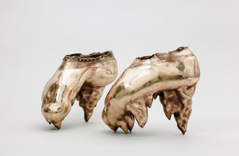 Zwei glänzende, skulpturale Objekte in Form von stilisierten Füßen mit unregelmäßigen Kanten und einer metallischen Oberfläche.