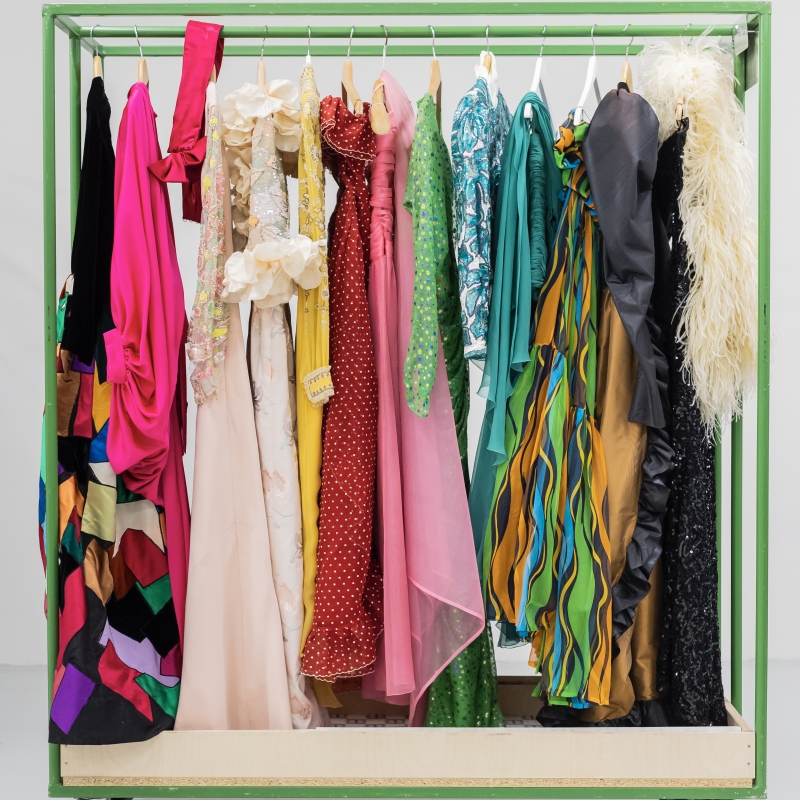 Bunte Kleider in verschiedenen Stilen hängen an einem grünen Kleiderständer.