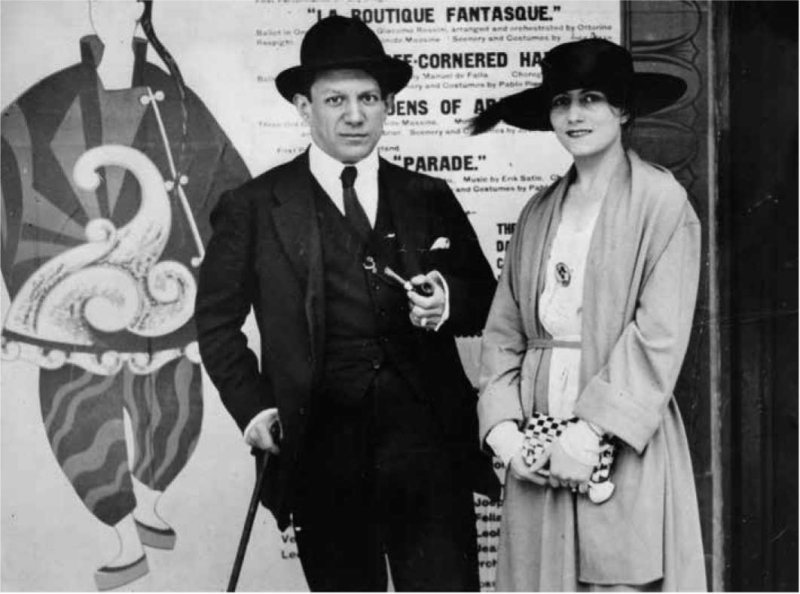 Pablo Picasso and a woman in stylish attire pose in front of a colorful theatrical poster featuring a clown.