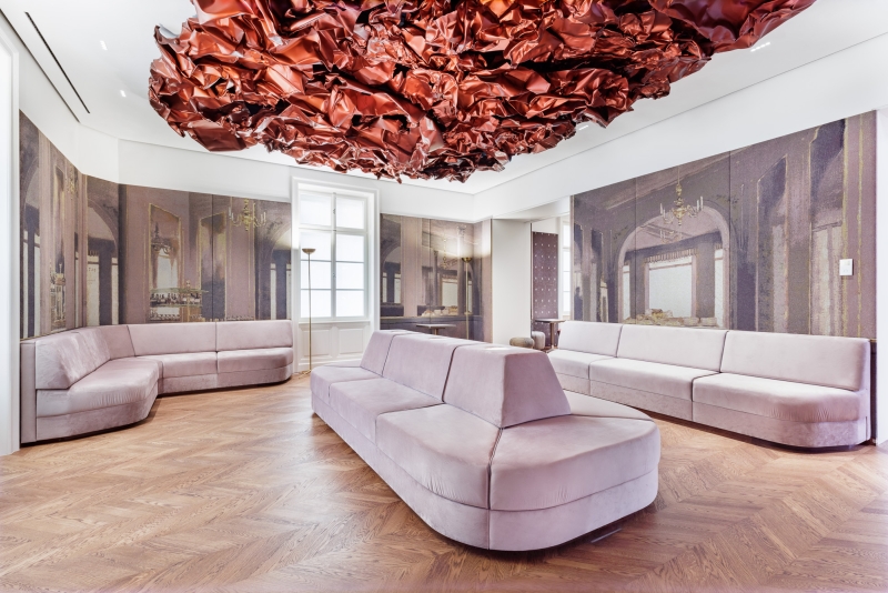 Modern lounge with pink sofas, a textured red ceiling installation, and wallpaper depicting elegant interiors.