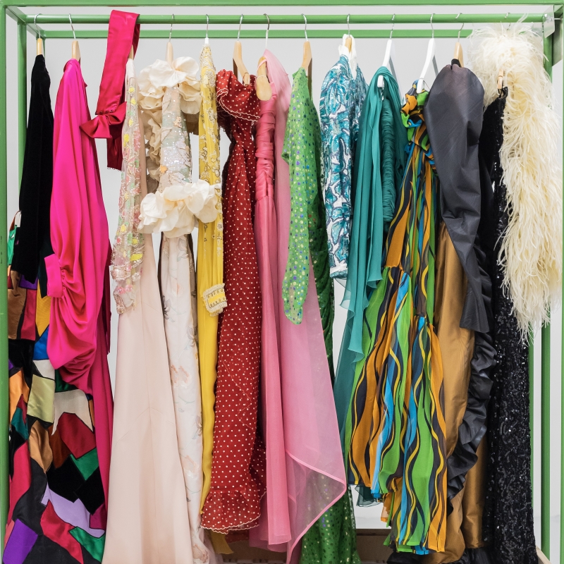 A rack displays a variety of colorful dresses in different styles, including sequined, polka-dotted, and patterned fabrics.