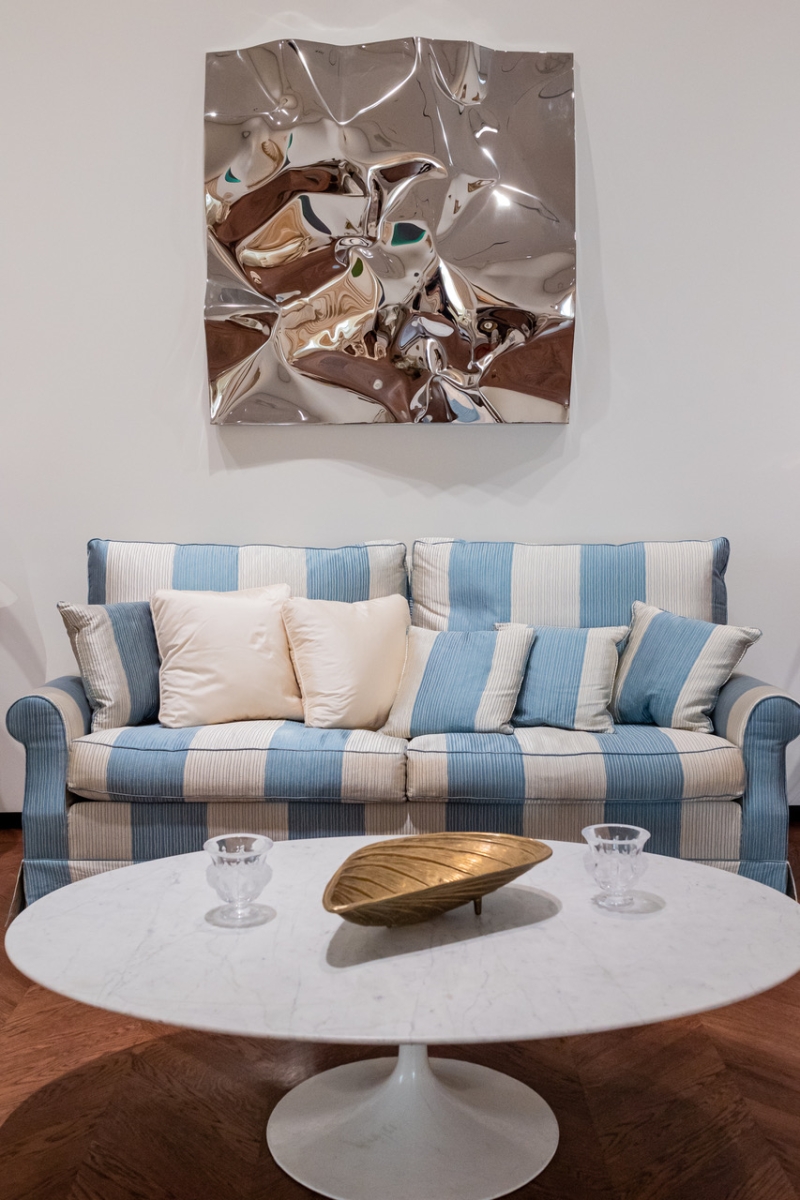 Gestreiftes Sofa mit Kissen, runder Marmortisch und glänzendem Wandkunstwerk.