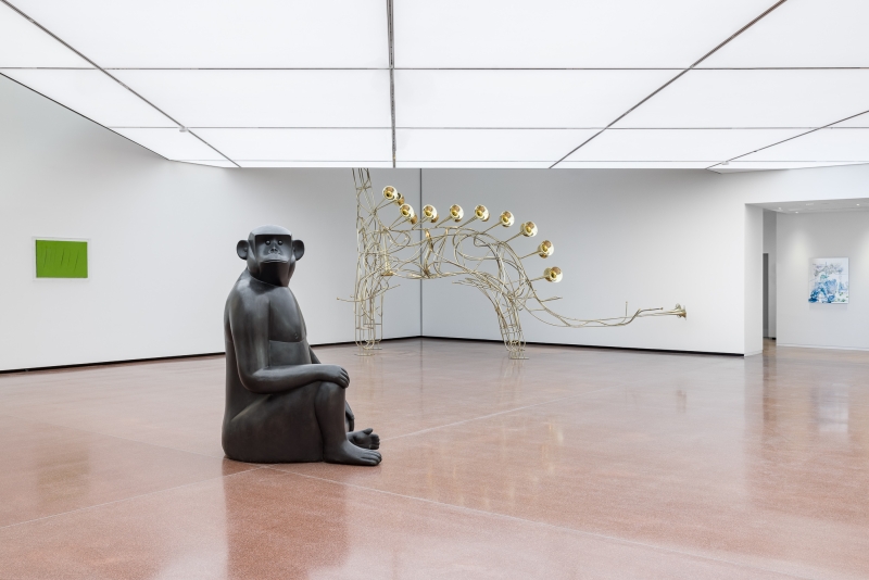 Schwarze Skulptur eines sitzenden Affen in einem modernen Ausstellungsraum mit Kunstwerken.