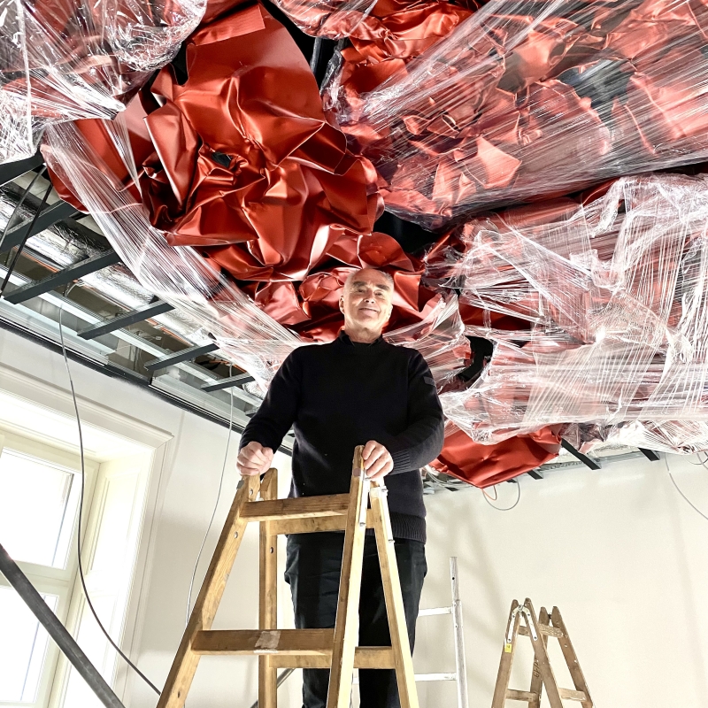 Mann auf einer Holzleiter in einem Raum mit rotem Deckenrelief.