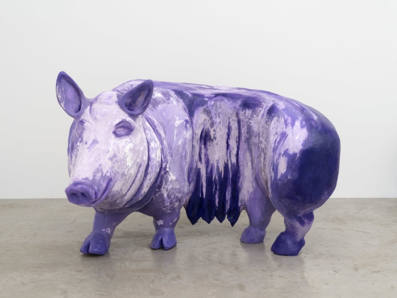 Lila Skulptur eines Schweins mit unregelmäßiger Farbstruktur auf grauem Boden.