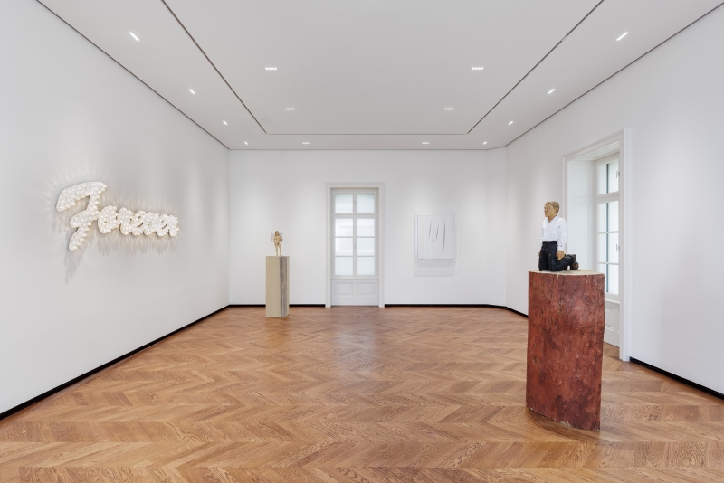 Helle Galerie mit Holzfußboden, Skulpturen und Kunstwerken an weißen Wänden, beleuchtet von Deckenstrahlern.