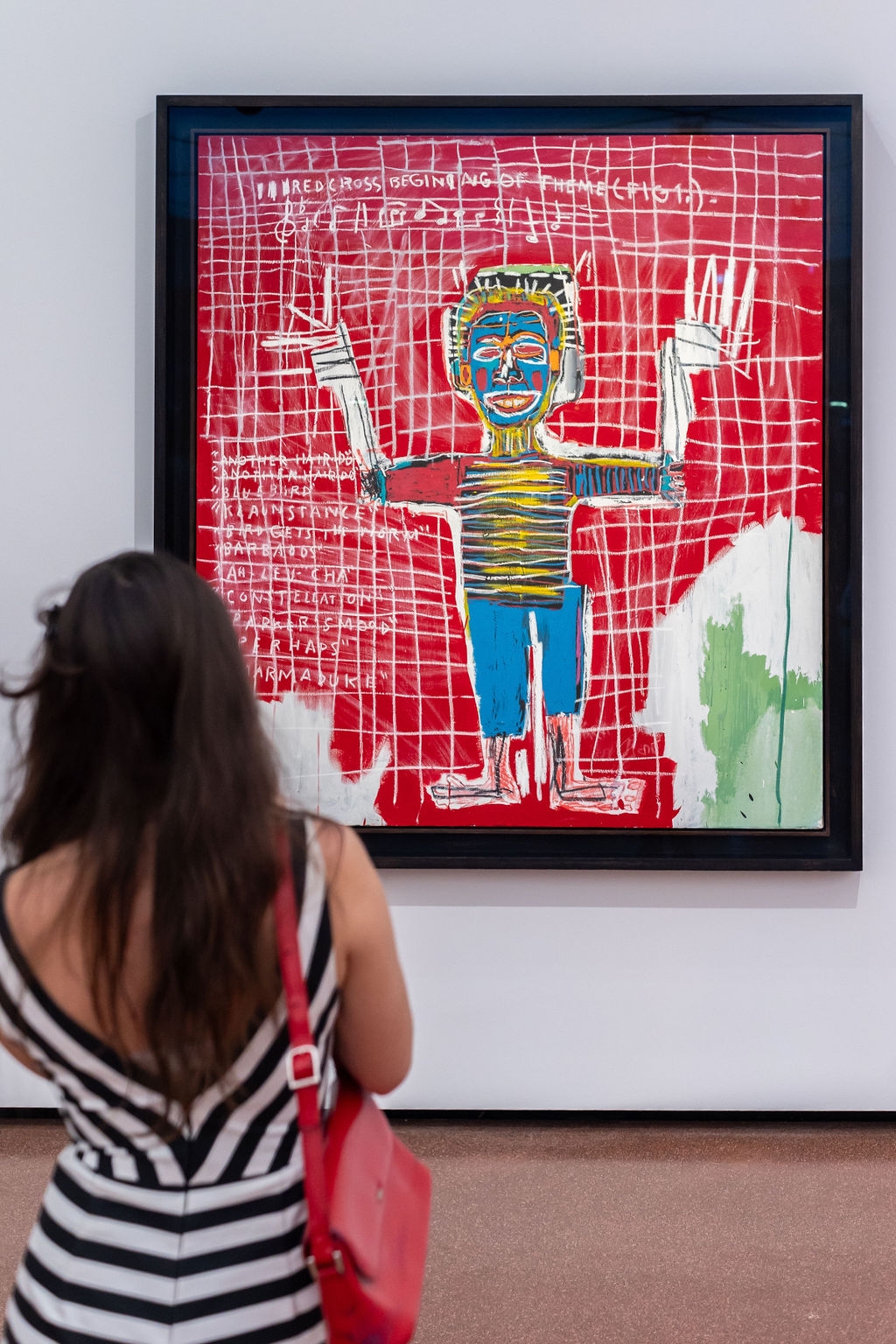 Eine Person betrachtet ein farbenfrohes Kunstwerk mit einer stilisierten Figur auf rotem Hintergrund.