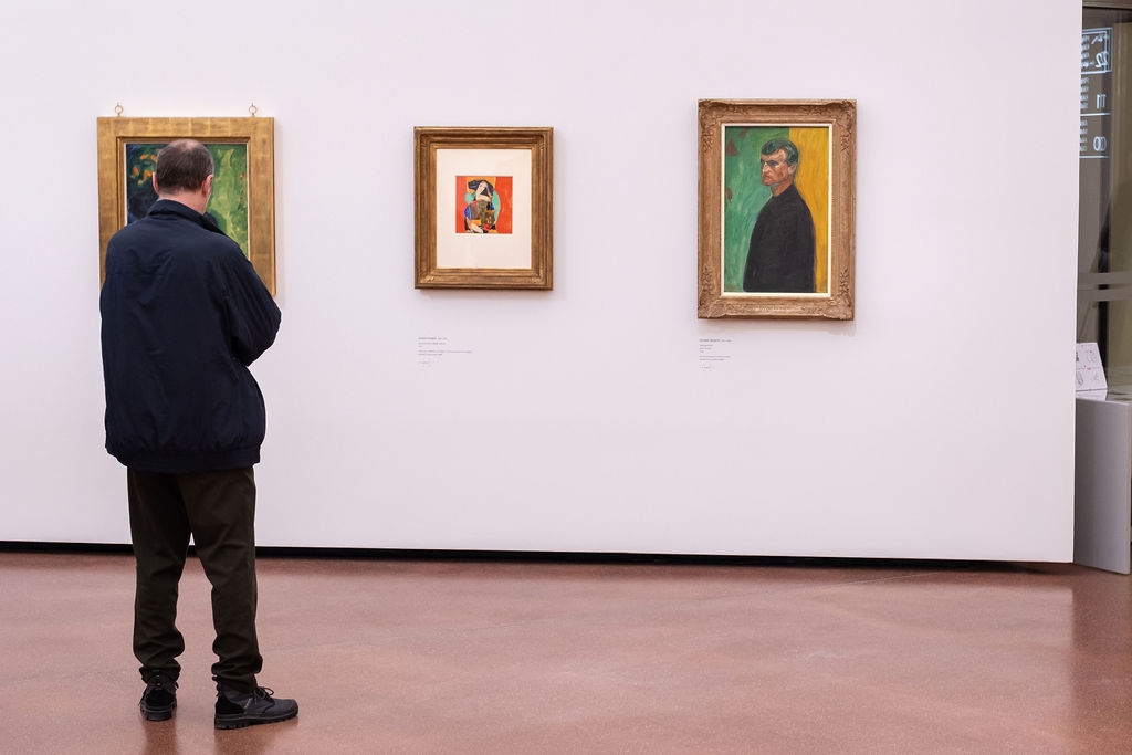 Mann betrachtet zwei Gemälde in einem modernen Ausstellungsraum mit weißen Wänden und glattem Boden.