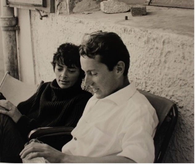 A young woman in a black sweater and a young man in a white shirt sit closely, engaged in conversation on a patio.
