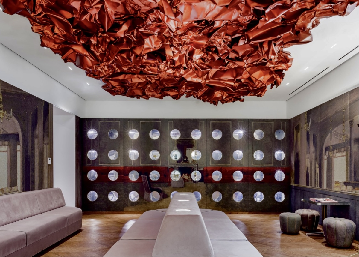 Roter, gewellter Deckenakzent über einem modernen Raum mit runder Wandgestaltung und eleganter Sitzgelegenheit.