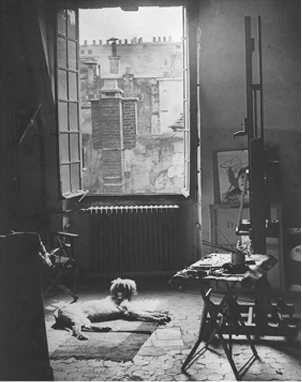 A sunlit artist's studio with a dog lying on the floor, an open window revealing a brick building outside.