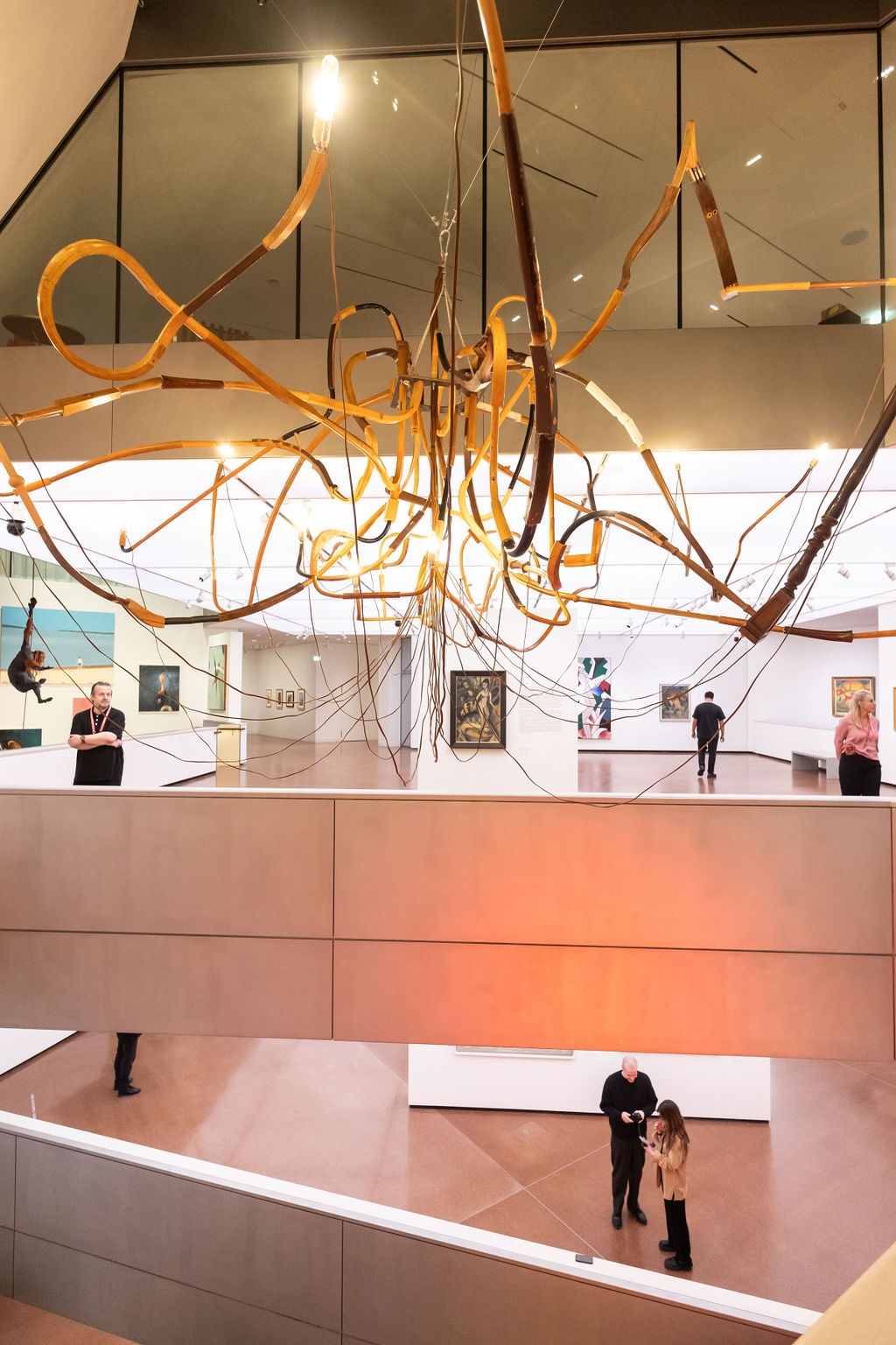 Moderne Galerie mit einer kunstvollen Deckeninstallation und Besuchern, die Gemälde betrachten.