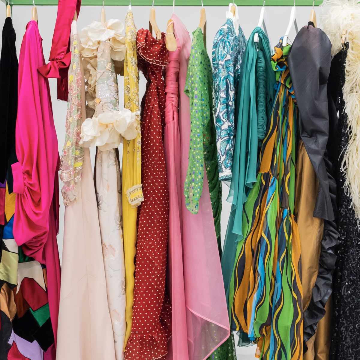 Bunte Kleider in verschiedenen Stilen und Texturen hängen an einer Kleiderstange.