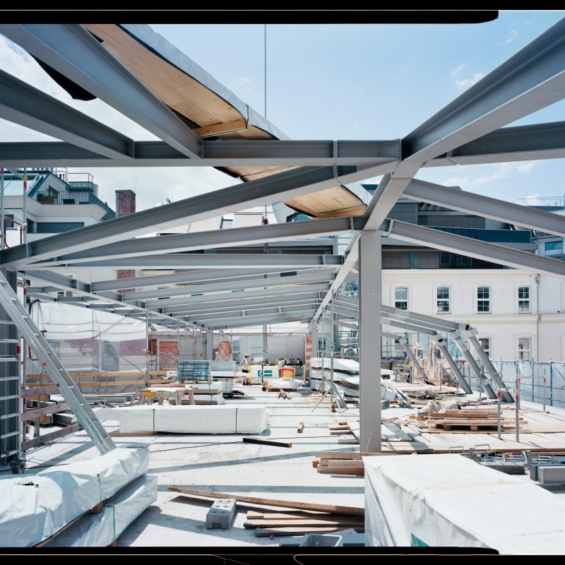 Baugerüst mit Stahlträgern, Baustellenmaterial und einem hellen Himmel im Hintergrund.