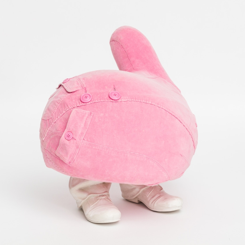 A round, pink sculpture resembling a cartoonish figure, wearing white shoes and featuring buttoned denim-like details.