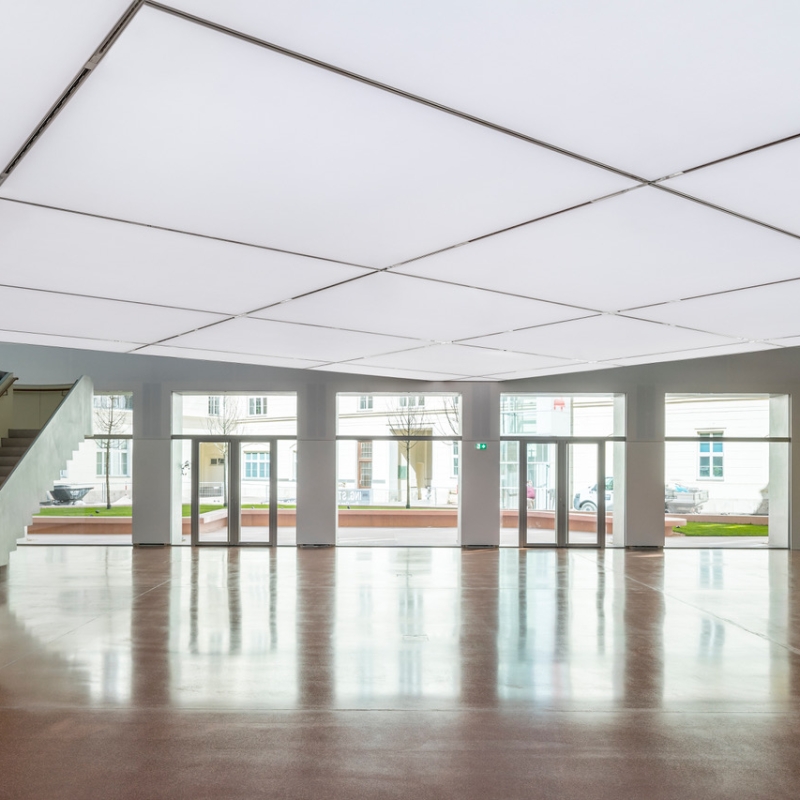 Spacious gallery interior with a bright ceiling, polished floor, and large windows revealing an outdoor view.