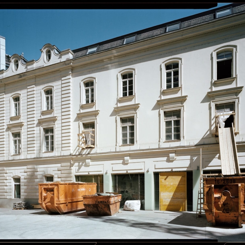 Renovation site featuring a historic building with construction debris and two orange dumpsters in front.